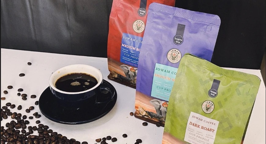 A cup of black coffee beside bags of Jowam coffee and roasted beans